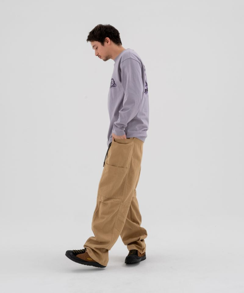 Model wearing beige Gramicci Voyager Pants and a lavender Gramicci Equipped Dirt Long-Sleeve-Tee on a light-tone background.