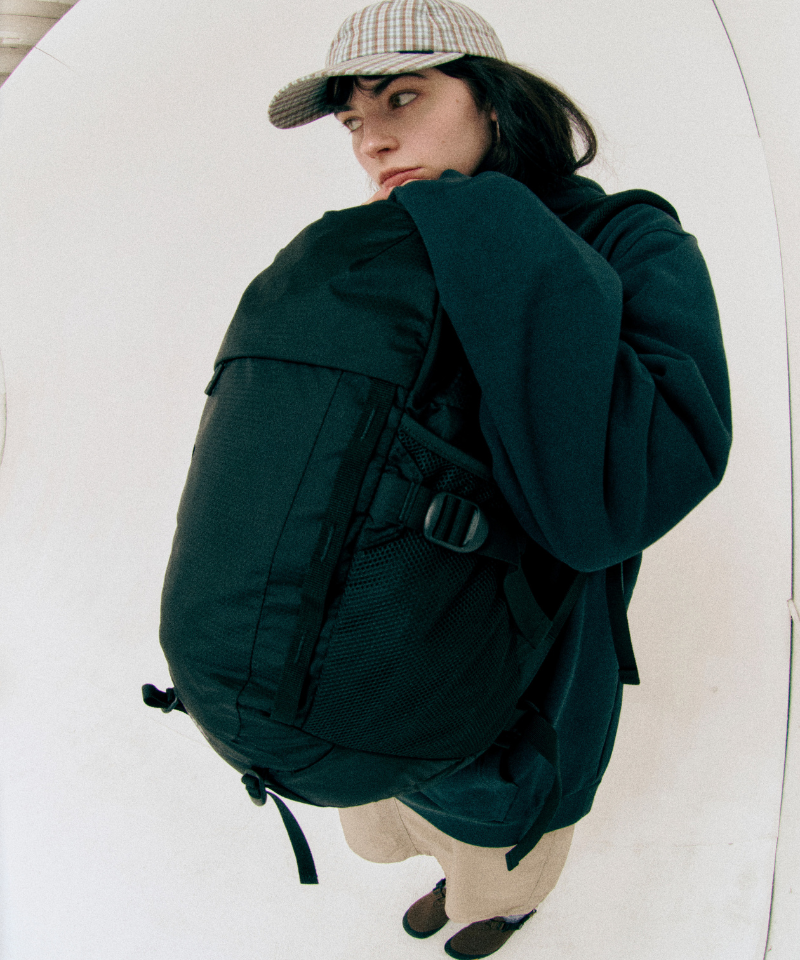 Model wearing green Gamicci Day Pack 25L and a green hoodie on a light-tone background.