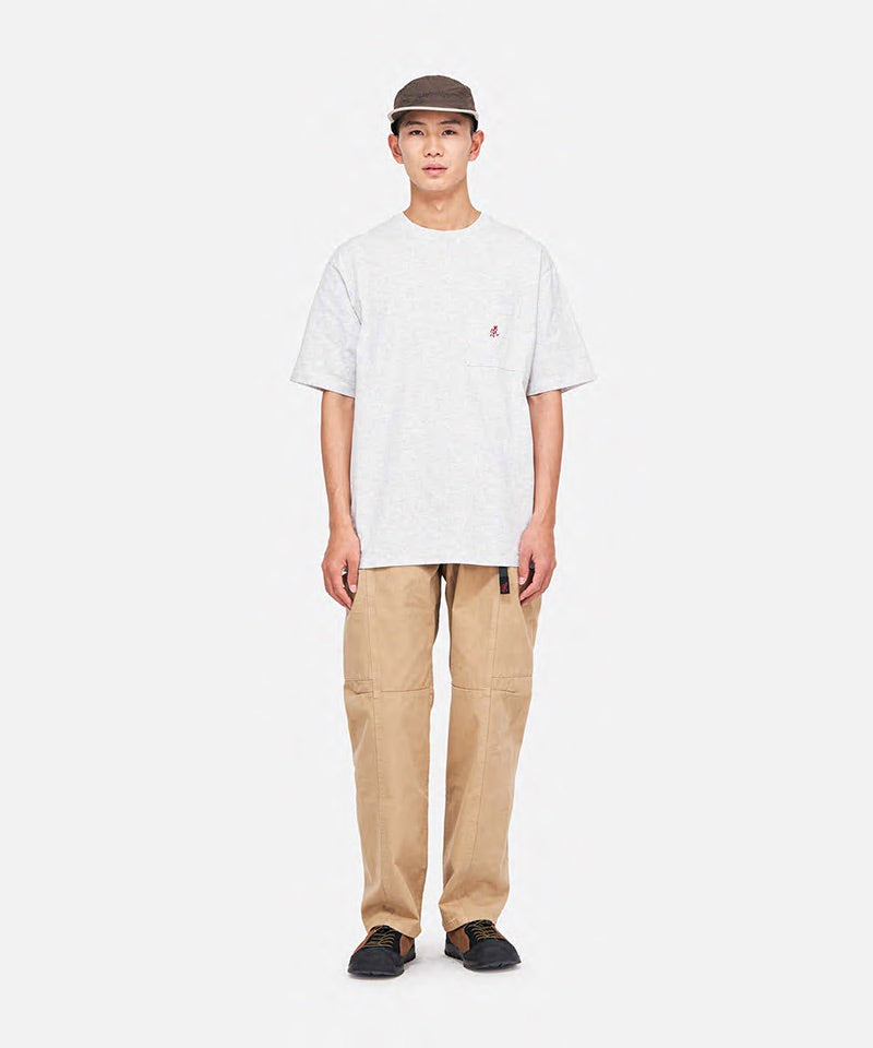 Model wearing a grey heather Gramicci One Point Tee with a small running man graphic and khaki pants on a light-tone background.