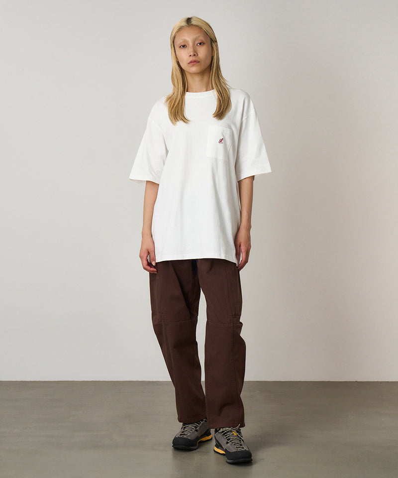 Model wearing a white Gramicci One Point Tee with a small running man graphic and brown pants on a light-tone background.