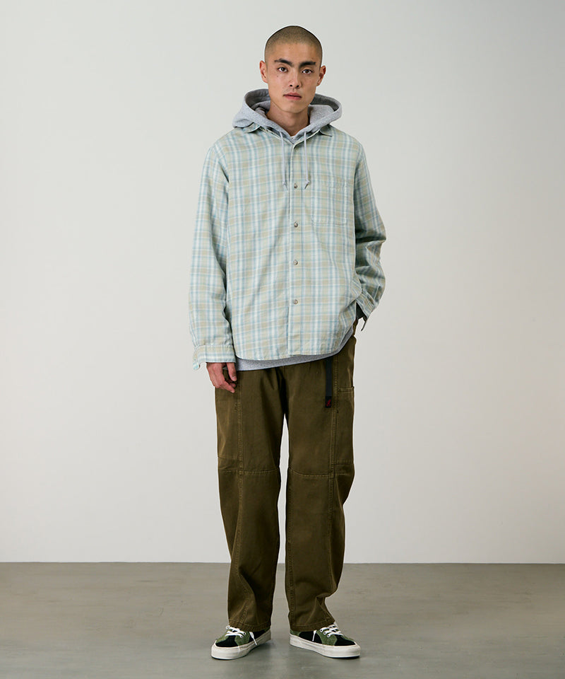 Model wearing bark pigment colored Gramicci Voyager Pants and a plaid jacket on a light-tone background.