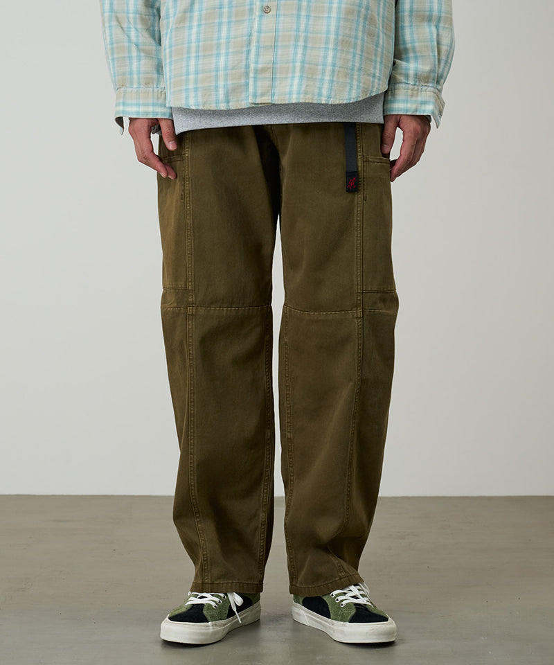Model wearing bark pigment colored Gramicci Voyager Pants and a plaid jacket on a light-tone background.
