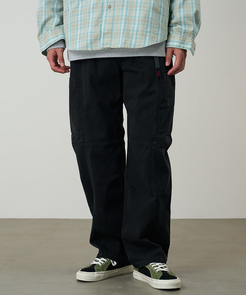 Model wearing black Gramicci Voyager Pants and a plaid jacket on a light-tone background.