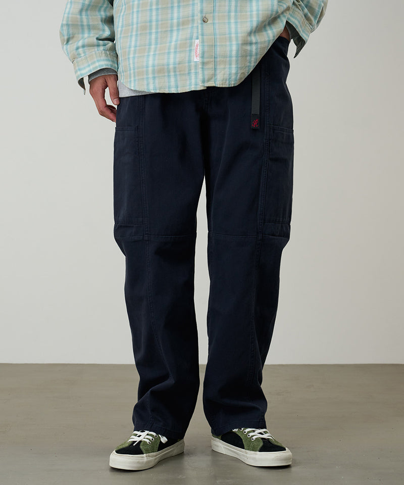 Model wearing double navy Gramicci Voyager Pants and a plaid jacket on a light-tone background.