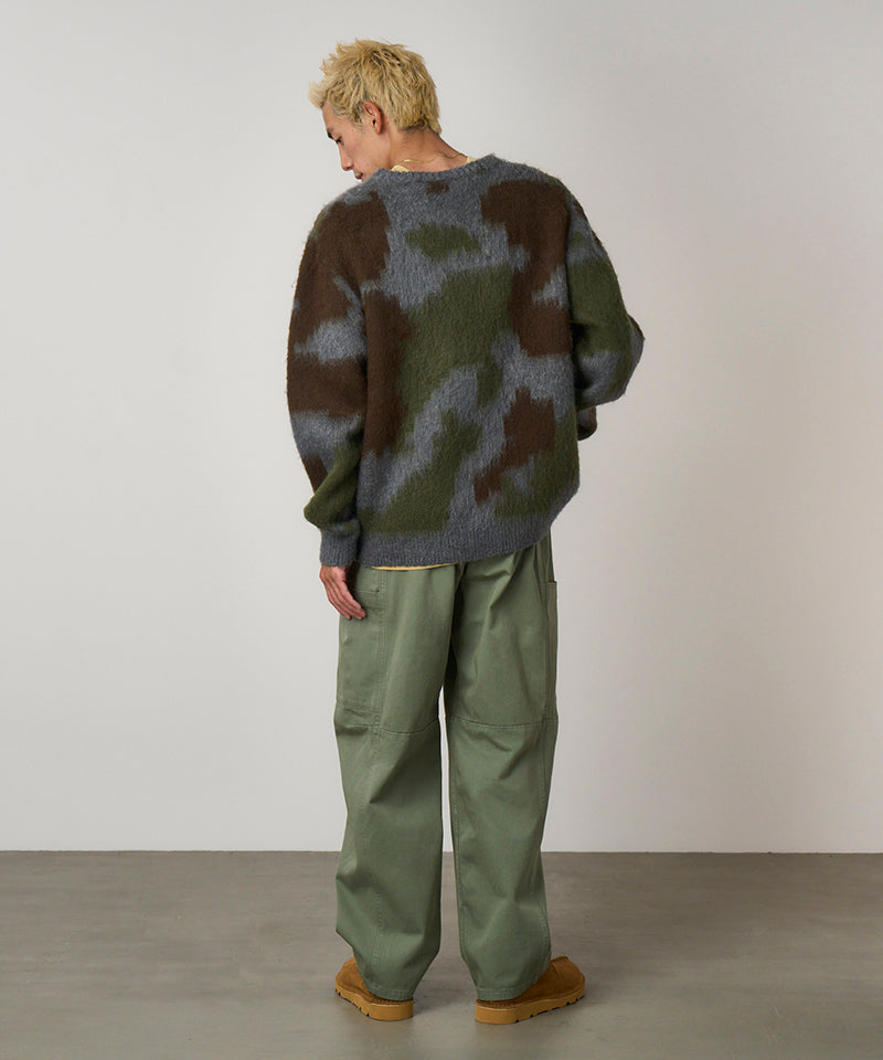 Back view of a model wearing sage colored Gramicci Voyager Pants and a mohair sweater on a light-tone background.