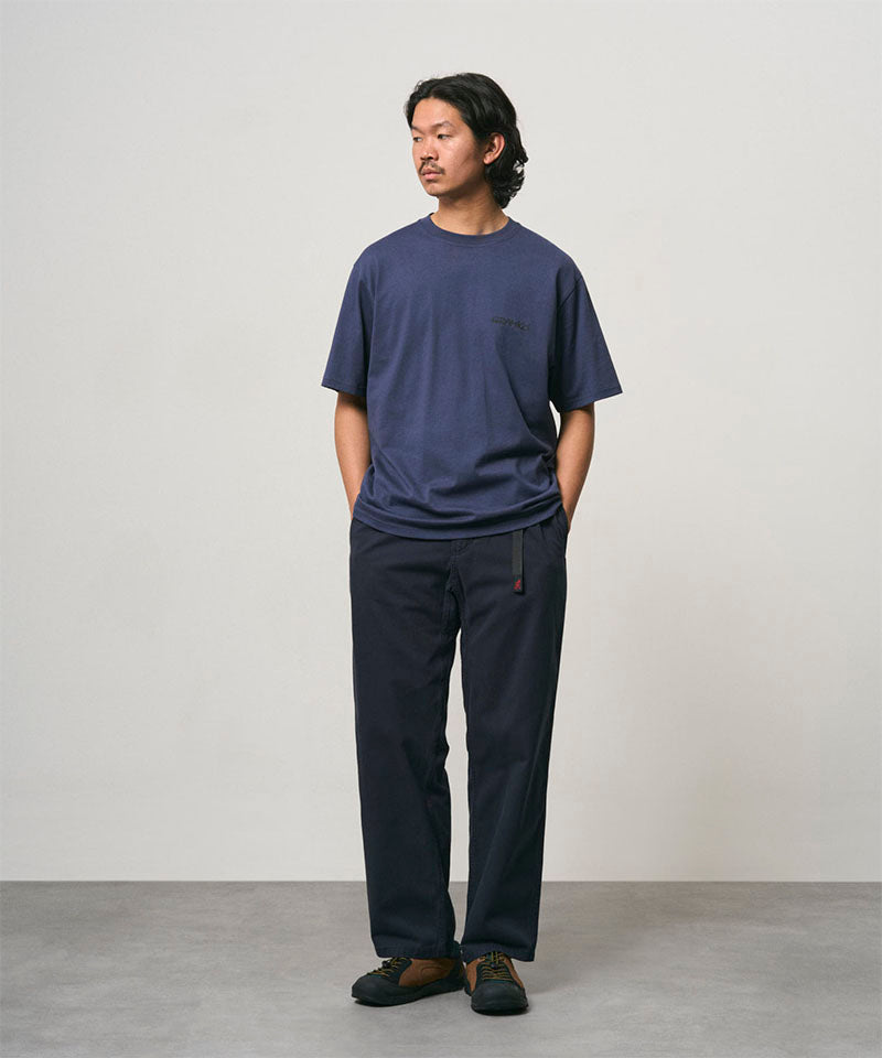 Model wearing a navy Gramicci Bass Tee and black pants on a light-tone background.