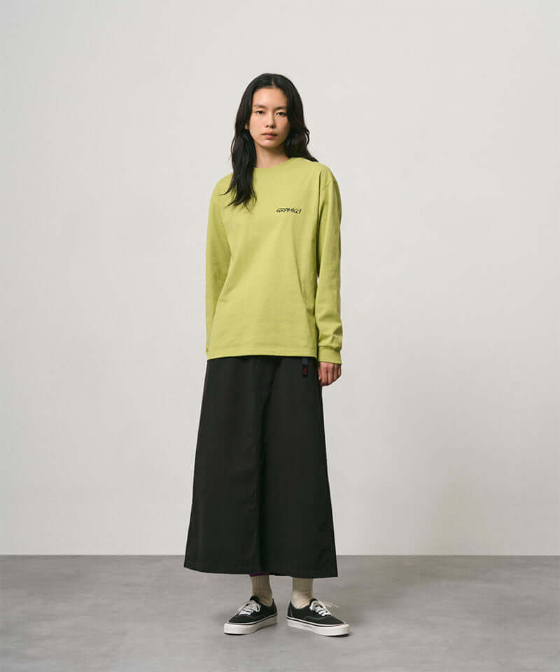 Model wearing a sweet pea colored Gramicci Bass Long-Sleeve Tee and black skirt on a light-tone background.