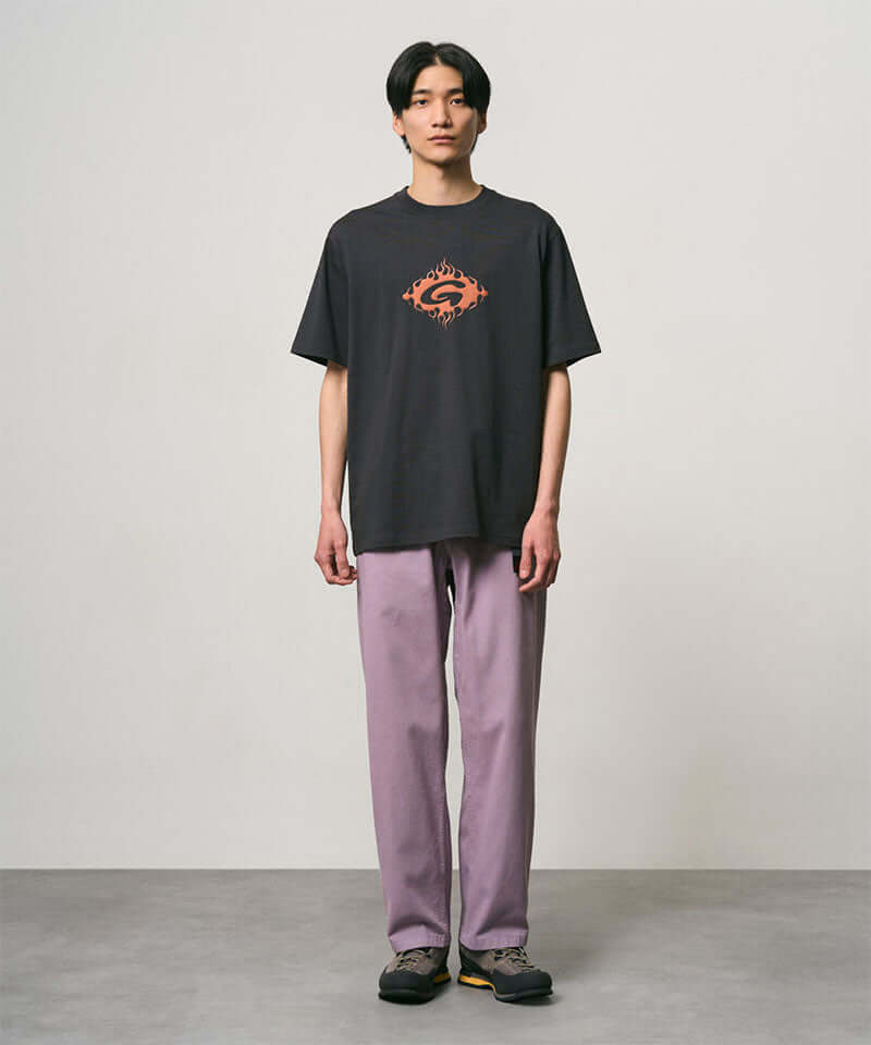 Model wearing a vintage black Gramicci Flames Tee with a graphic and lavender pants on a light-tone background.