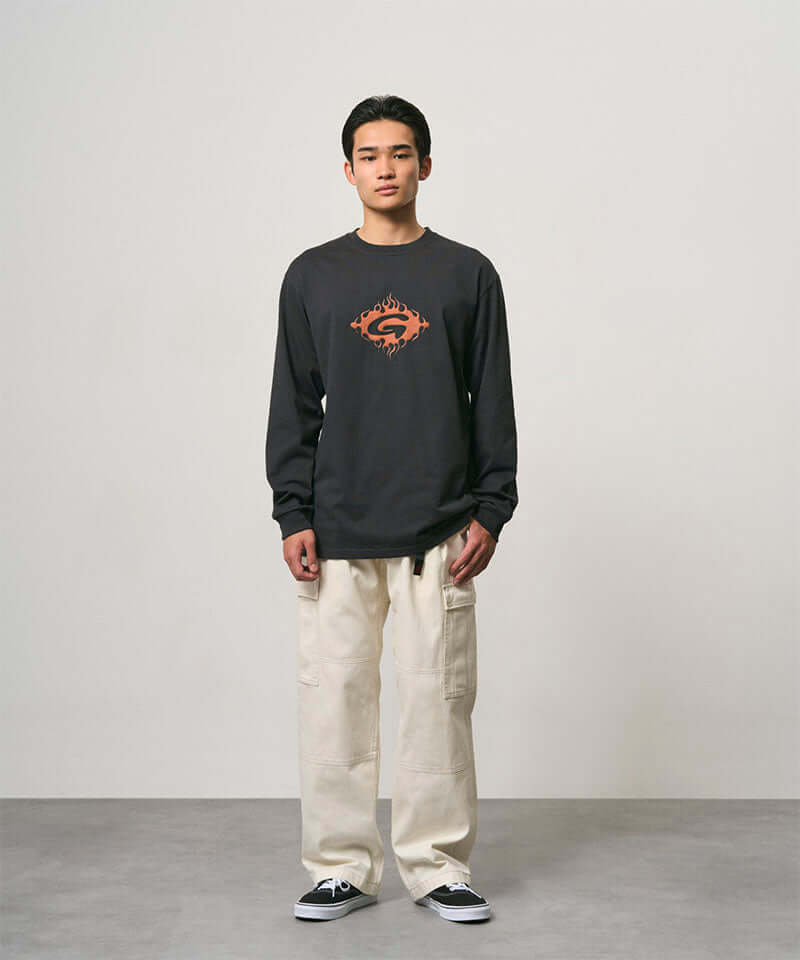 Model wearing a vintage black Gramicci Flames Long Sleeve Tee with a graphic and creme colored pants on a light-tone background.