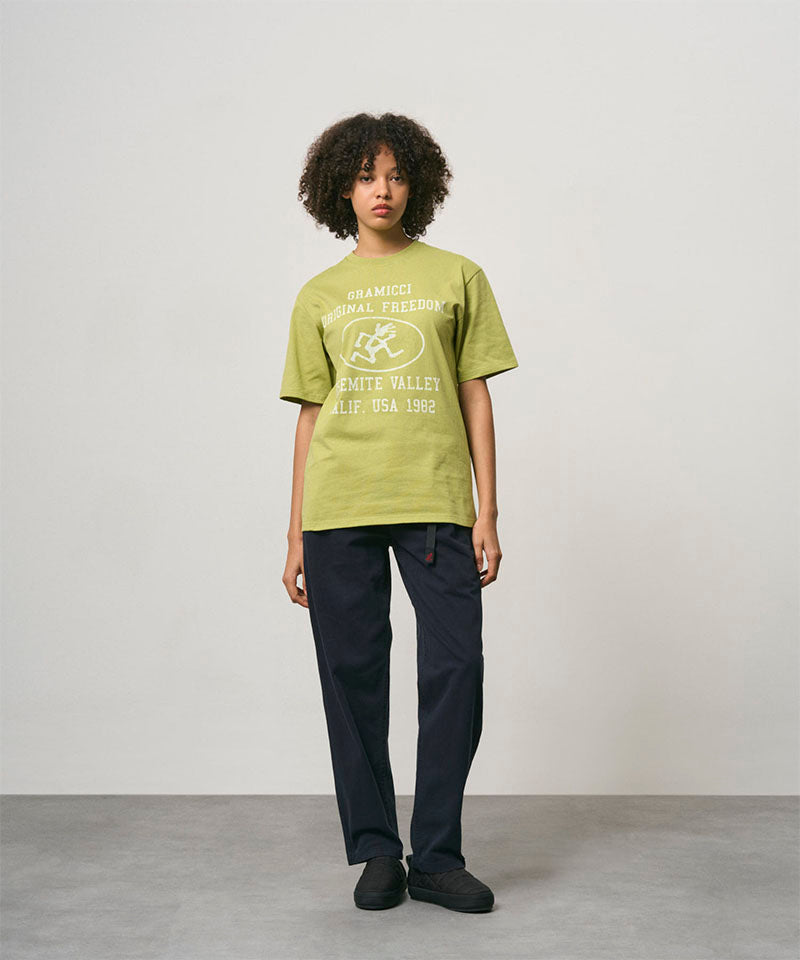 Model wearing a sweet pea colored Gramicci Yosemite Valley Tee with a graphic and black pants on a light-tone background.