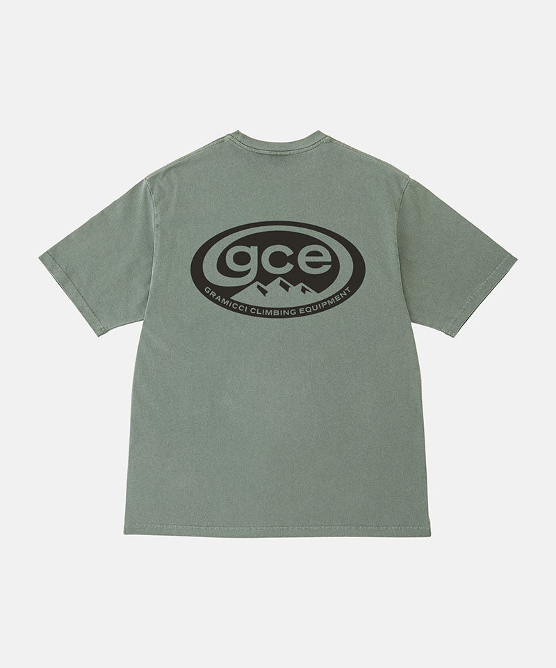 Back view of a Gramicci sage pigment colored GCE Tee Pigment Dyed with a graphic against a light-tone background.