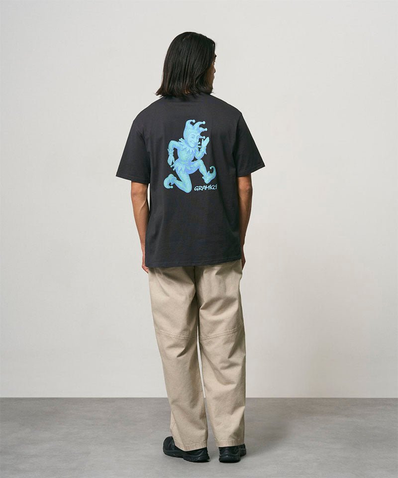 Back view of a model wearing a vintage black Gramicci Joker Tee with a teal graphic and beige pants on a light-tone background.