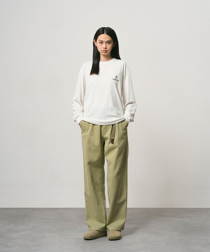 Model wearing a white Gramicci One Point Logo Long Sleeve Tee with a graphic and light olive pants on a light-tone background.