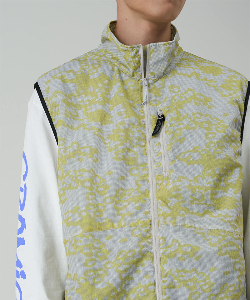 Model wearing a Gramicci yellow and grey grid camo Flyweight Vest against a light-tone background.
