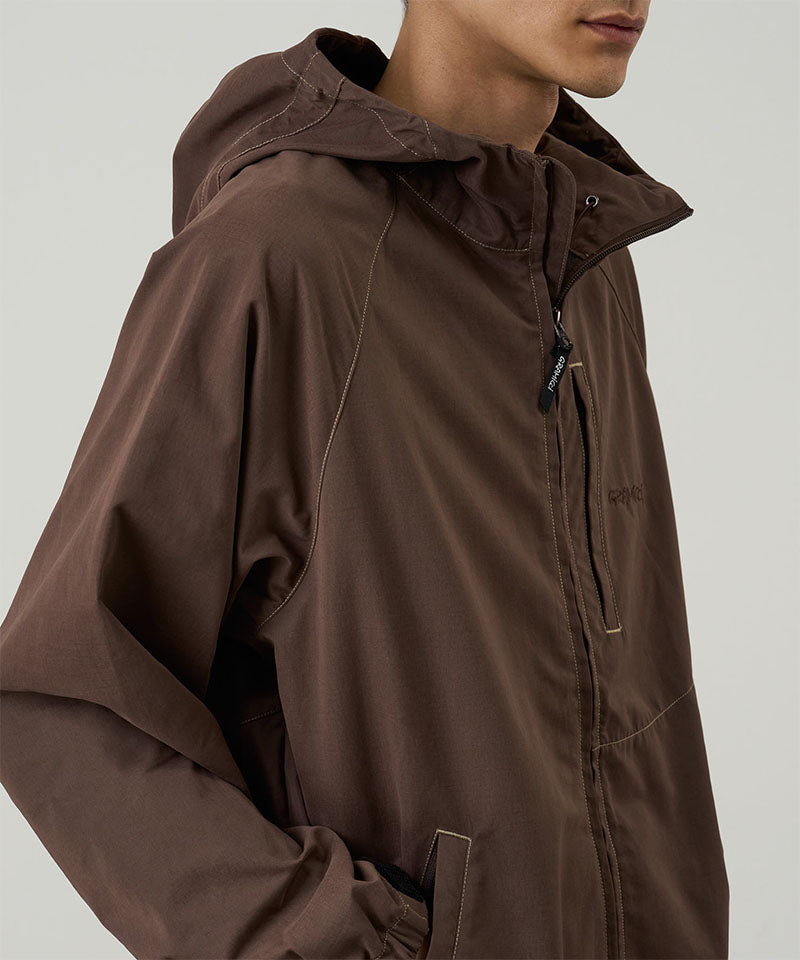 Model wearing a Gramicci walnut colored Milton Hooded Jacket against a light-tone background.