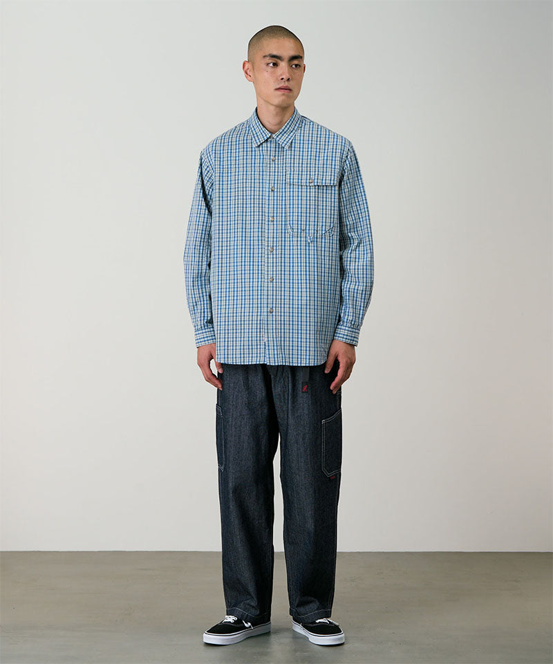 Model wearing a blue plaid Gramicci Poplin Millwood Shirt and blue pants on a light-tone background.