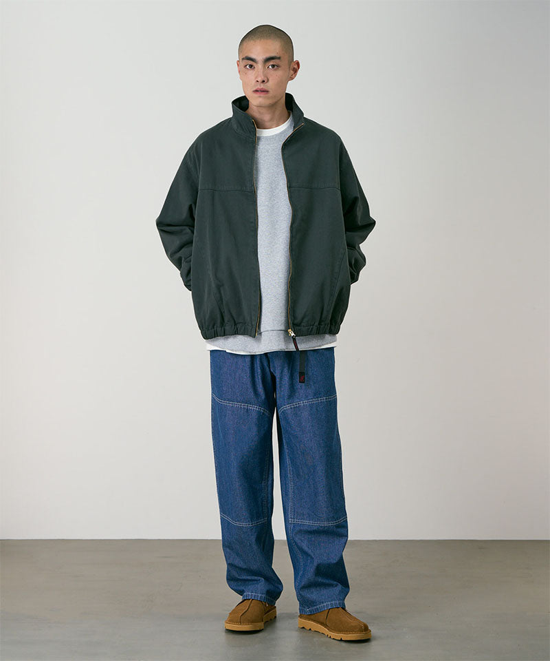 Model wearing the Gramicci Japanese Chambray Double Knee pant in blue and a dark green jacket on a light tone background.