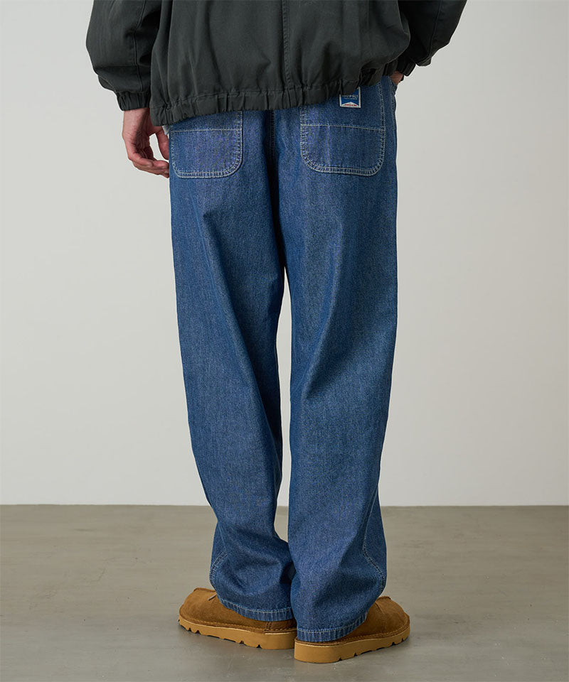 Rear view of a model wearing the Gramicci Japanese Chambray Double Knee pant in blue on a light tone background.