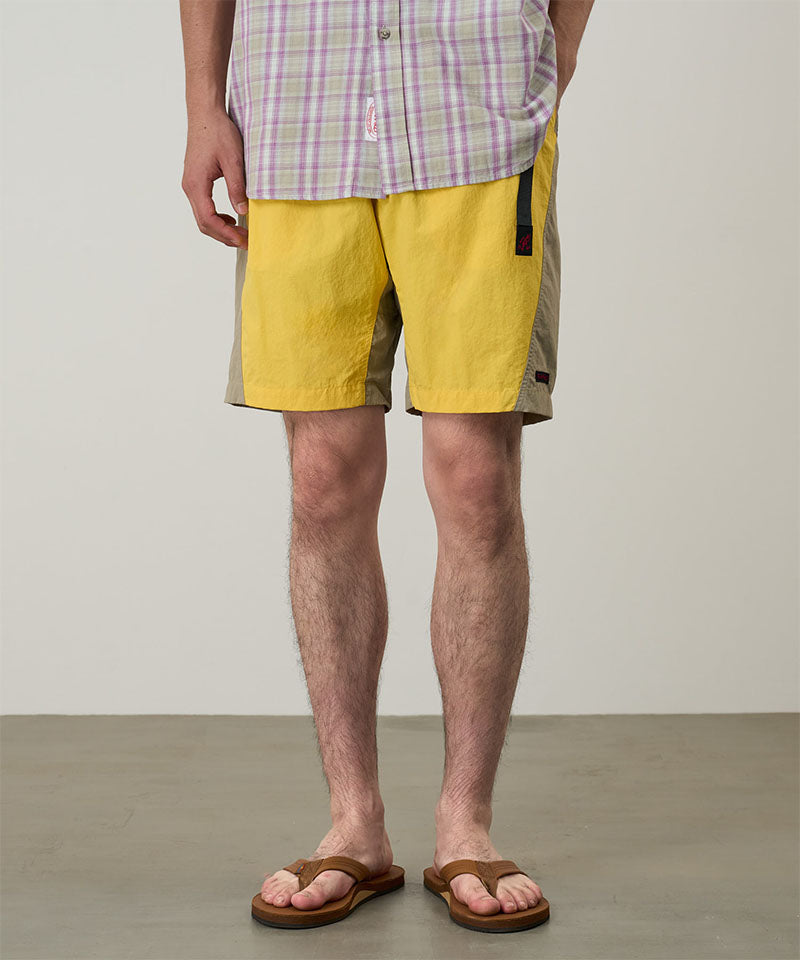 Model wearing banana colored Gramicci Nylon Block Shorts and a purple plaid shirt on a light-tone background.