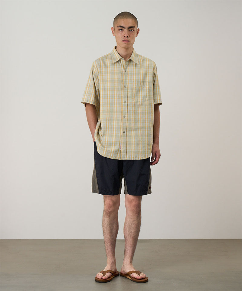 Model wearing black Gramicci Nylon Block Shorts and a yellow plaid shirt on a light-tone background.
