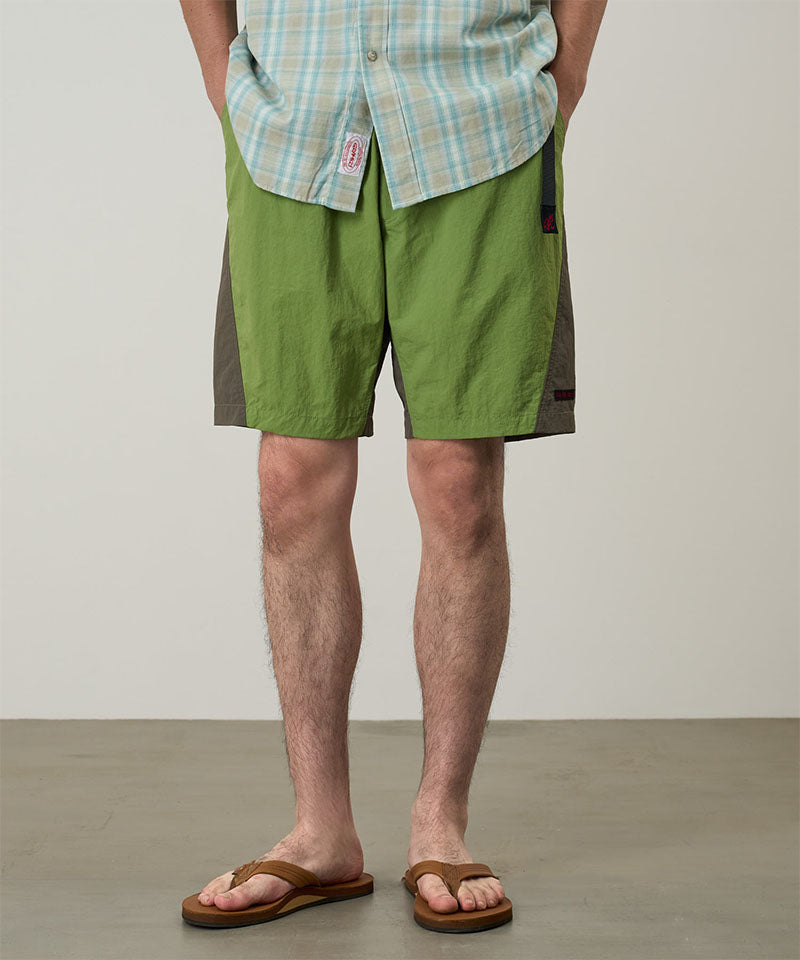 Model wearing jade green Gramicci Nylon Block Shorts and a green plaid shirt on a light-tone background.