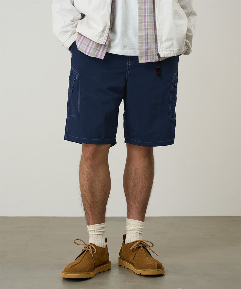 Model wearing british navy Gramicci Nylon Cliff Short and a white jacket on a light-tone background.