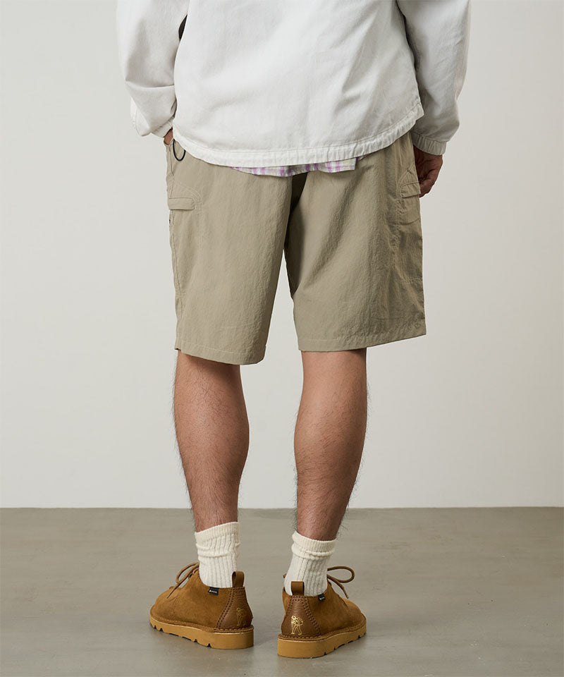Back view of a model wearing milk tea colored Gramicci Nylon Cliff Short and a white jacket on a light-tone background.