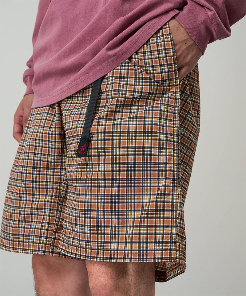 Model wearing brick check colored Gramicci Checkered Shell Shorts and a red shirt on a light-tone background.