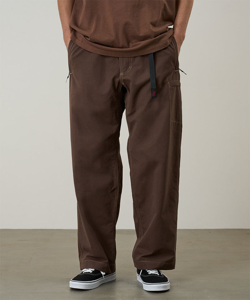 Model wearing walnut Gramicci Milton Pants and a brown shirt on a light-tone background.