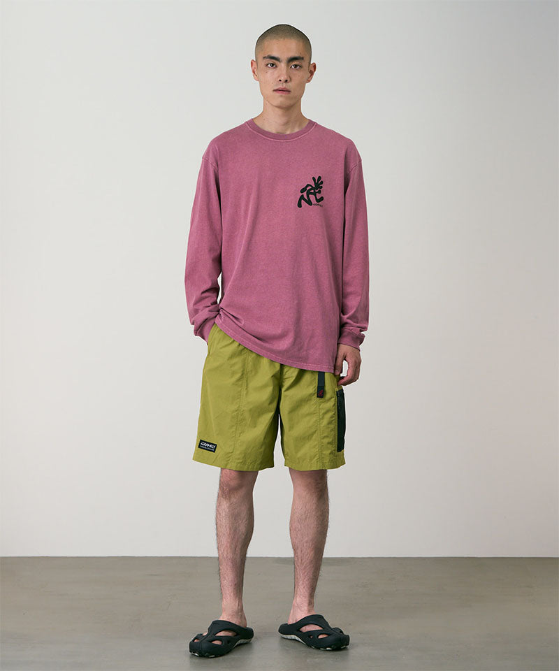 Model wearing field green Gramicci Guide Shorts and a red shirt on a light-tone background.
