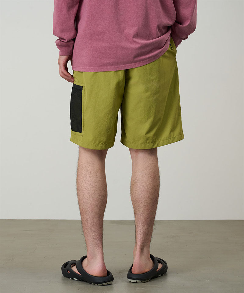 Back view of a model wearing field green Gramicci Guide Shorts and a red shirt on a light-tone background.
