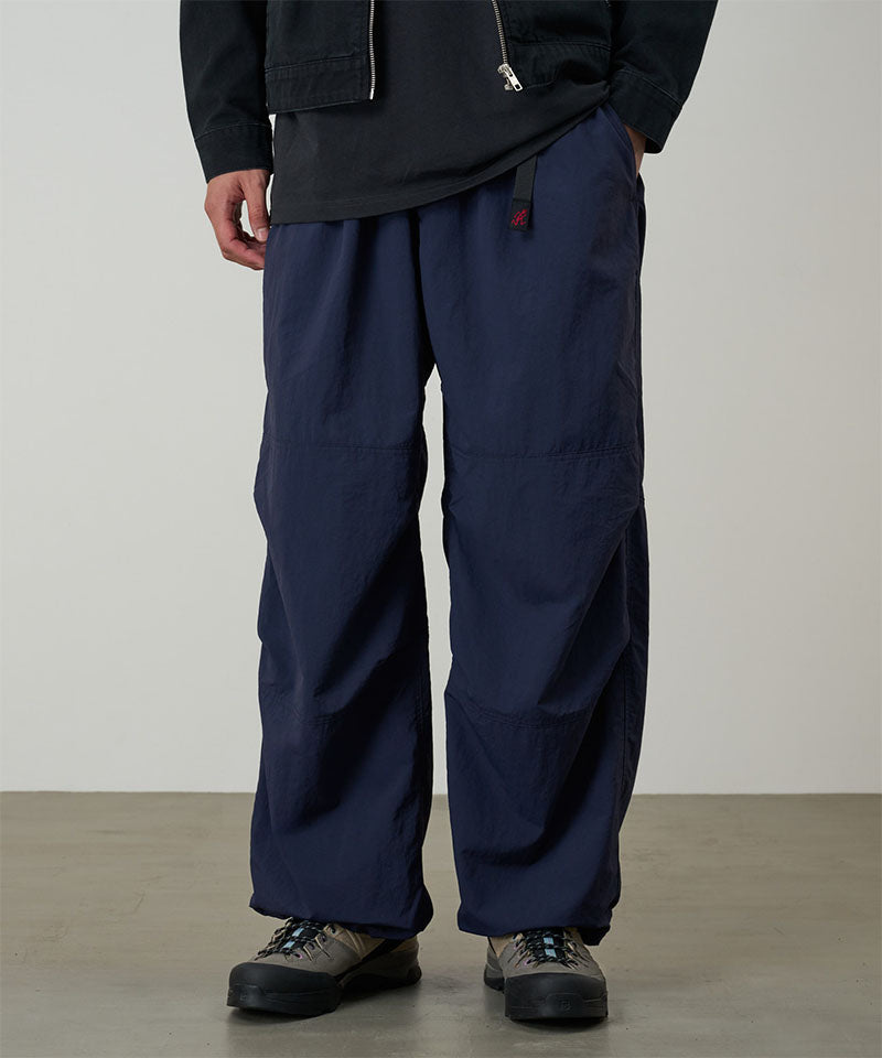 Model wearing british navy Gramicci Nylon Paneled Trek Pants and a black jacket on a light-tone background.