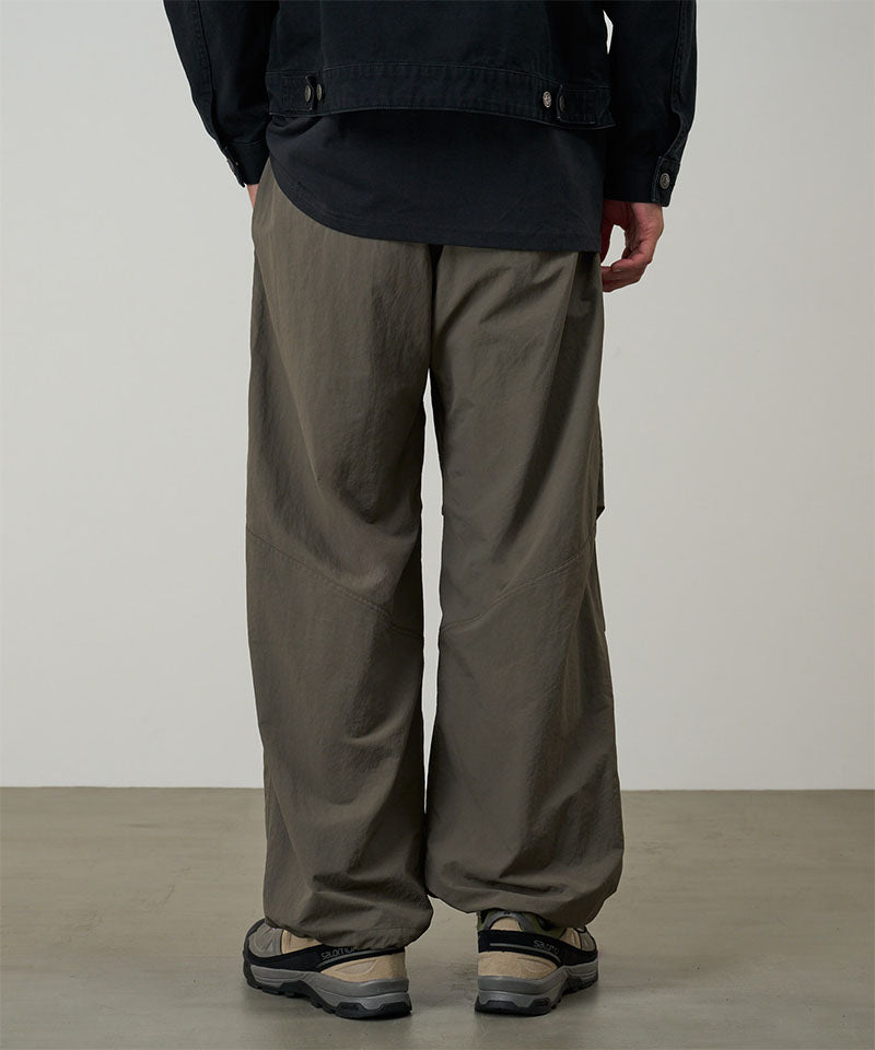 Back view of a model wearing granite colored Gramicci Nylon Paneled Trek Pants and a black jacket on a light-tone background.