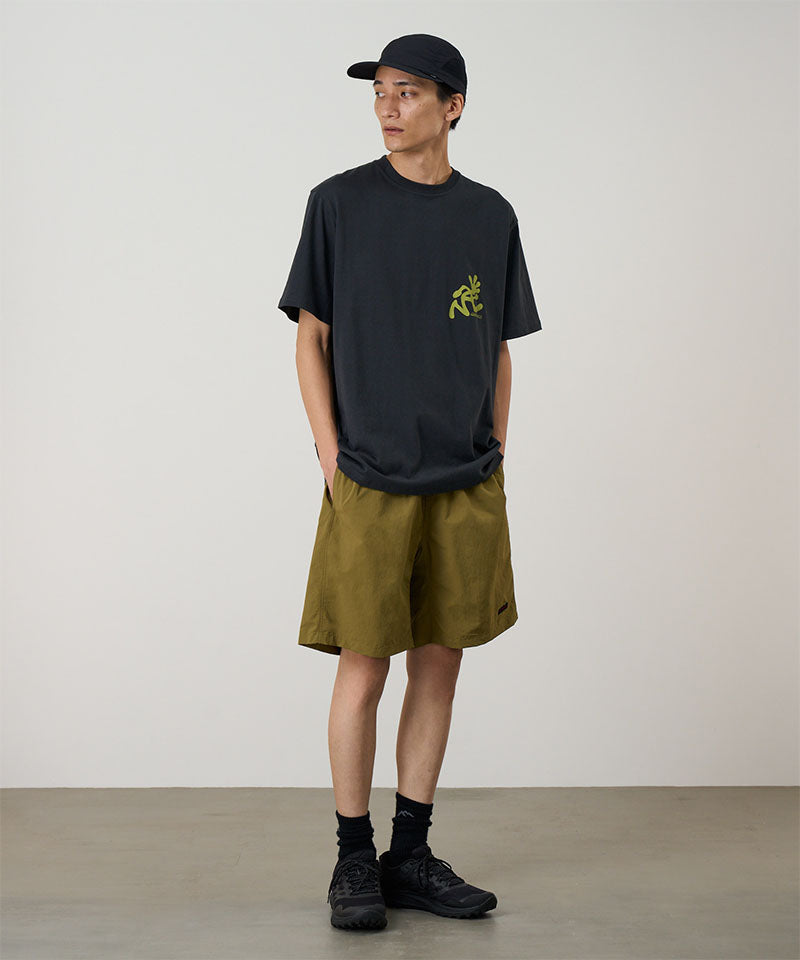 Model wearing artichoke colored Gramicci Nylon Reef Shorts and a black shirt on a light-tone background.