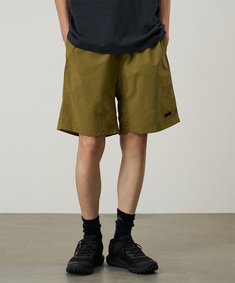 Model wearing artichoke colored Gramicci Nylon Reef Shorts and a black shirt on a light-tone background.