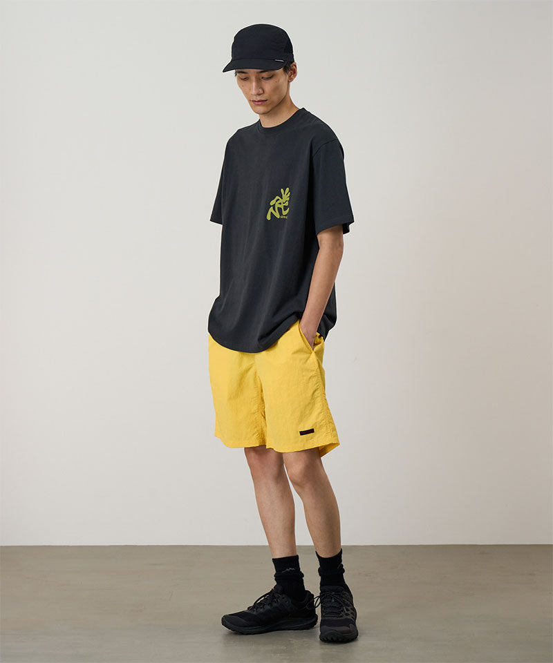 Model wearing a banana colored Gramicci Nylon Reef Short and a black shirt on a light-tone background.