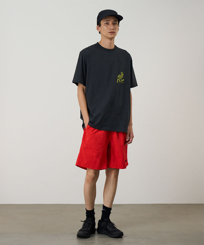 Model wearing burnt orange Gramicci Nylon Reef Shorts and a black shirt on a light-tone background.