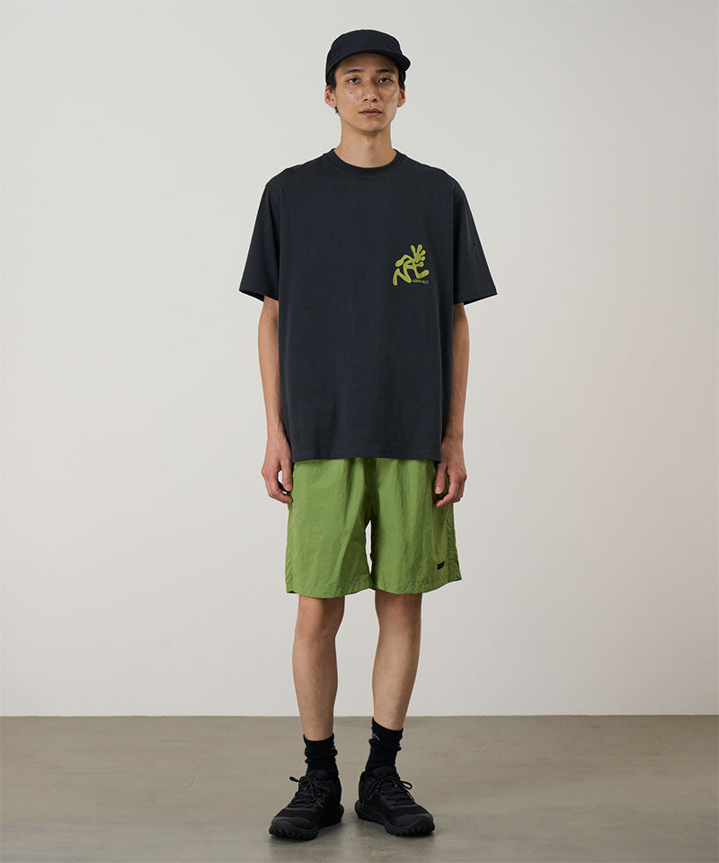 Model wearing jade green Gramicci Nylon Reef Shorts and a black shirt on a light-tone background.
