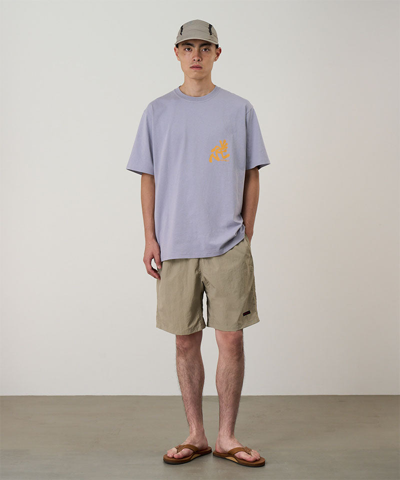 Model wearing milk tea colored Gramicci Nylon Reef Shorts and a lavender shirt on a light-tone background.