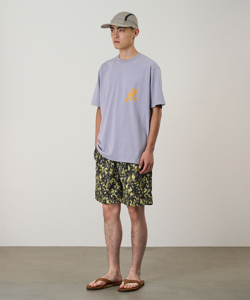 Model wearing olive camo Gramicci Nylon Reef Shorts and a lavender shirt on a light-tone background.