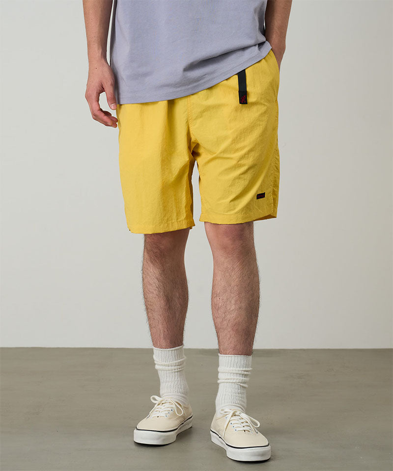 Model wearing banana colored Gramicci Nylon Packable G-Shorts and a lavender shirt on a light-tone background.