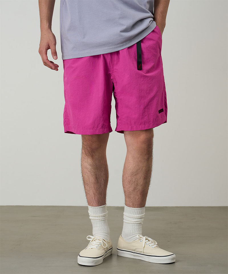 Model wearing bright plum colored Gramicci Nylon Packable G-Short and a lavender shirt on a light-tone background.