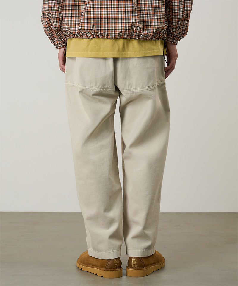 Back view of a model wearing sand pigment Gramicci EQT Pant and a plaid jacket on a light-tone background.