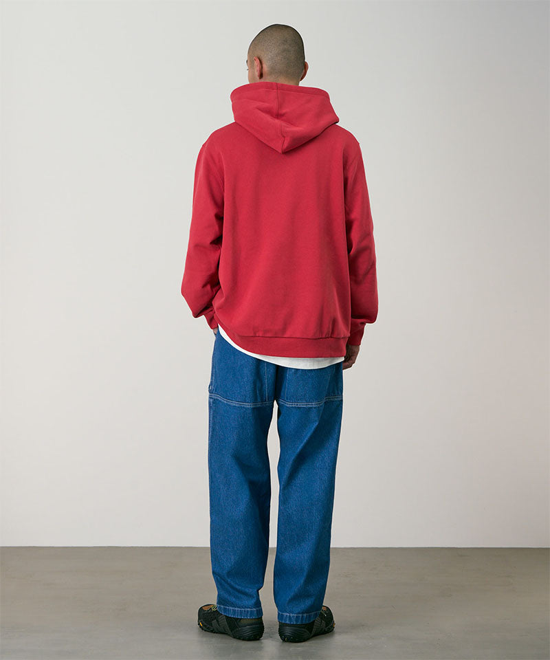 Back view of a model wearing light wash colored Gramicci Denim EQT Pant and a red hoodie on a light-tone background.