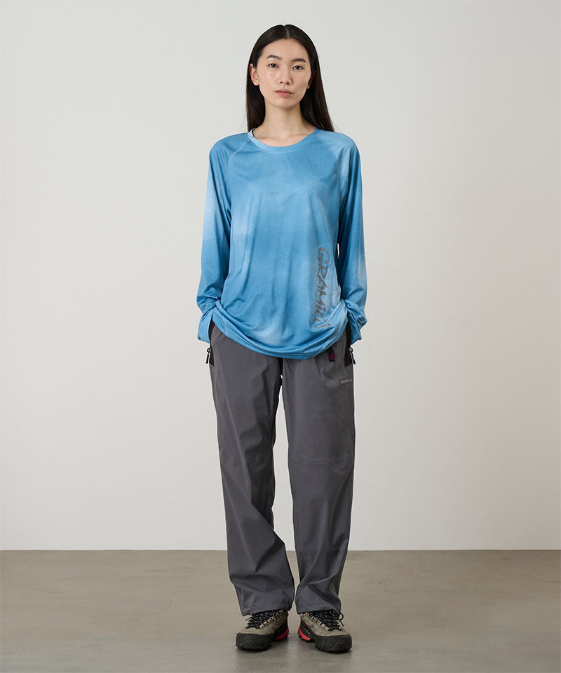 Model wearing a blue tie-dye Gramicci L/S 1st Layer shirt with grey graphic and grey pants on a light-tone background.