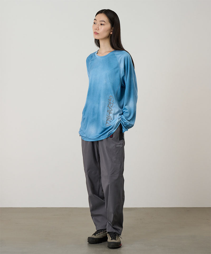 Model wearing a blue tie-dye Gramicci L/S 1st Layer shirt with grey graphic and grey pants on a light-tone background.