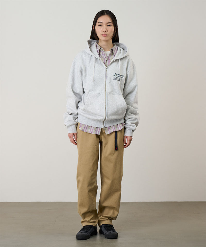 Model wearing a heather ash Gramicci G-Sail Zip Hooded Sweatshirt with a teal graphic and khaki pants on a light-tone background.