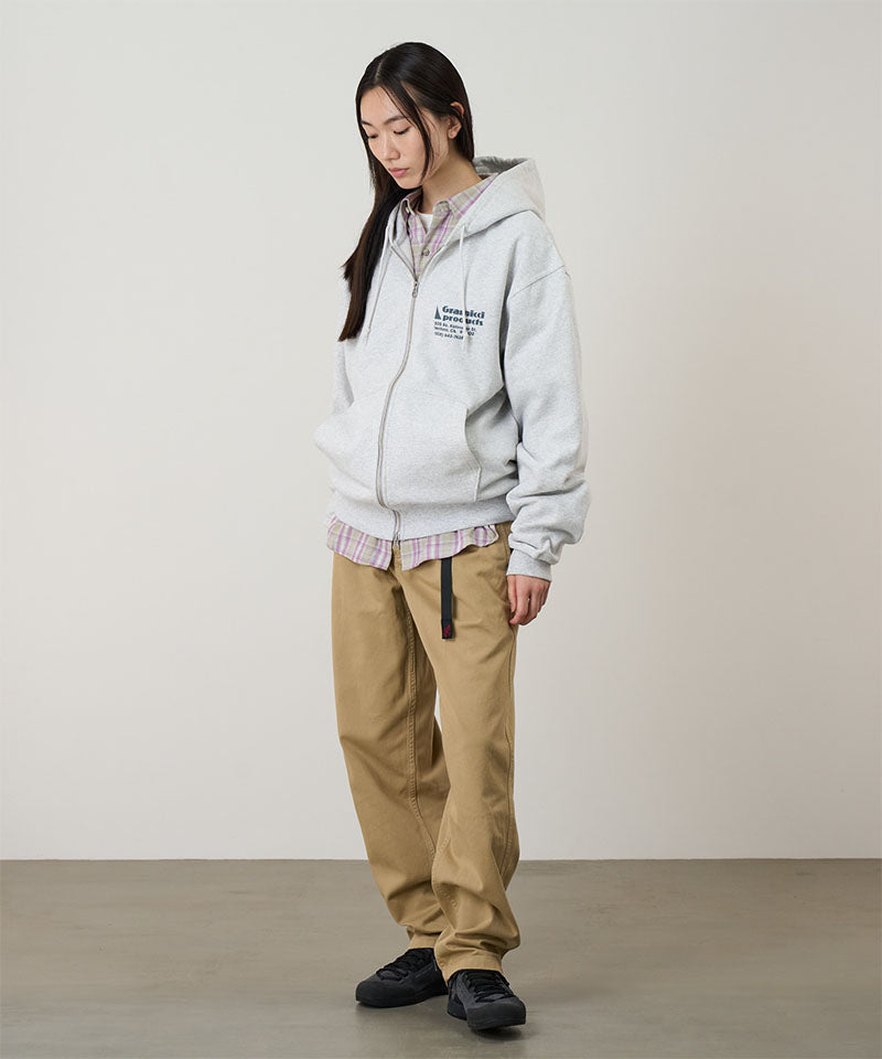 Model wearing a heather ash Gramicci G-Sail Zip Hooded Sweatshirt with a teal graphic and khaki pants on a light-tone background.