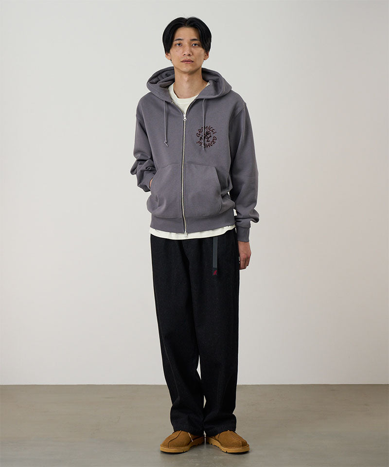 Model wearing charcoal Gramicci Running Man Zip Hooded Sweatshirt and a black pants on a light-tone background.