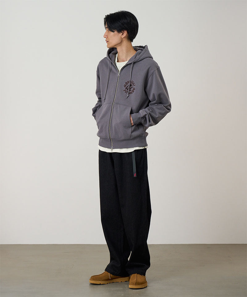 Model wearing charcoal Gramicci Running Man Zip Hooded Sweatshirt and a black pants on a light-tone background.